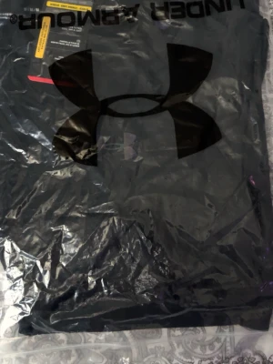 Svart Under Armour t-shirt - Snygg svart t-shirt från Under Armour med stort logotryck på bröstet. Tillverkad i mjukt och lätt material som passar perfekt till träning eller chill. Klassisk passform och korta ärmar gör den enkel att matcha med allt.