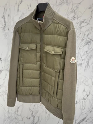 Olivgrön cardiganjacka från Moncler - Snygg olivgrön cardiganjacka från Moncler med quiltad front och två stora bröstfickor med lock. Ärmar och sidor i stickad bomull, ribbad krage och muddar. Dragkedja framtill och klassisk Moncler-logga på ärmen.