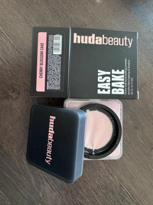 Huda Beauty Easy Bake Cherry Blossom - Löspuder från Huda Beauty i nyansen Cherry Blossom Cake. Kommer i en svart plastburk med rosa text och tillhörande kartong. Pudret är ljusrosa och passar perfekt för baking och fixering av makeup. Praktisk förpackning som är enkel att ta med.
