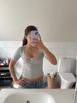 Randig croppad topp - Säljer en vit och svart randig croppad topp med korta ärmar och en djup urringning. Toppen har en slim passform och är perfekt till jeans eller kjol. Materialet känns mjukt och stretchigt.