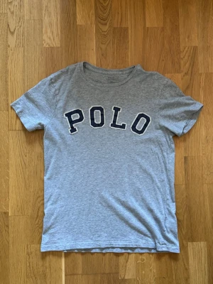 Ralph Lauren T-shirt - Strl M, Slim Fit. 100% bomull. Klassisk grå T-shirt med broderad Polo Ralph Lauren-logga på bröstet. Okej begagnat skick med två små hål vid axeln (se bild). I övrigt fint skick. 