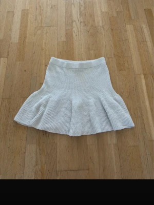 Vit stickad kortkjol med volang - Supersöt vit stickad kortkjol med volangkant. Kjolen har en mjuk och stretchig midja och är perfekt för dig som gillar en feminin och trendig stil. Passar till både sneakers och boots.