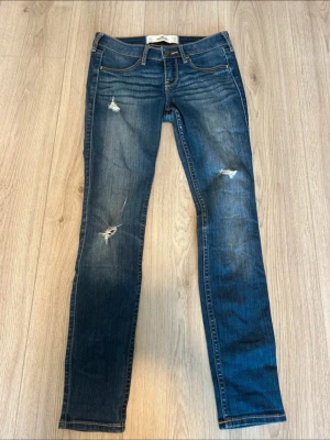 Blå slitna jeans från hollister  - Säljer ett par blå skinny jeans från hollister med slitningar och hål på benen för en trendig look. . Materialet är stretchigt denim som sitter tajt och bekvämt.