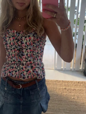 Blommig axelbandslös topp - Söt axelbandslös topp med blommigt mönster i rosa, rött, blått och grönt. Toppen har volangkant nedtill och längs överkanten samt rynkade detaljer framtill. Perfekt för varma dagar och ger en romantisk vibe.