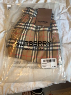 Burberry shorts  - Klassiska rutiga shorts från Burberry i beige, svart, vit och röd. Ikoniskt Burberry-mönster med elastisk midja och avslappnad passform. Perfekta för dig som vill ha en tidlös och trendig look. xs men är stora i storlek så passar s och m