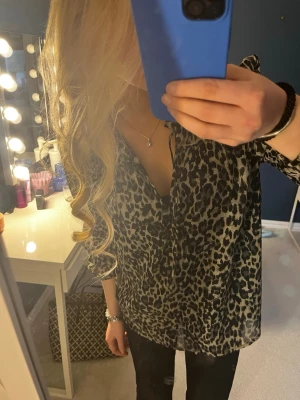Leopardmönstrad blus med v-ringning - Nypris 599. Snygg blus med leopardmönster i svart och beige toner. Blusen har v-ringning och långa ärmar med knapp vid ärmslut. Materialet ser lätt och luftigt ut, perfekt för att skapa en trendig look. Passar till både jeans och kjol. 