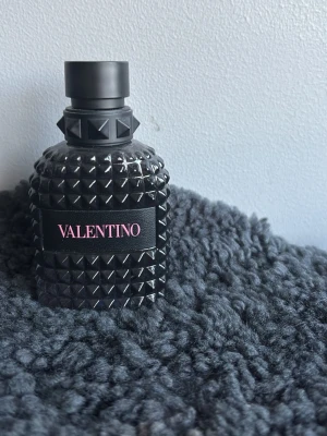 Valentino svart parfymflaska - Säljer en snygg parfym från Valentino i en svart, nitat glasflaska med cool design. Flaskan har en matt svart kork och etikett med Valentino-loggan i rosa. Perfekt för dig som gillar exklusiva och stilrena dofter. 42 milliliter born in Roma 