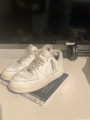 Vita Nike Air Force 1 sneakers - Klassiska vita Nike Air Force 1 sneakers i lågt utförande. Skorna har en stilren design med perforerad tå, vita skosnören och Nike Swoosh på sidorna. Tillverkade i läder med gummisula och diskret AIR-detalj på hälen. Perfekta för en clean och tidlös look.