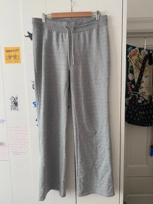 Grå mjukisbyxor med vida ben - Säljer ett par klassiska grå mjukisbyxor med vida ben och dragsko i midjan. Byxorna har en enkel och clean look, perfekta för chill dagar hemma eller när du vill vara bekväm. Tillverkade i mjukt material som känns skönt mot huden.