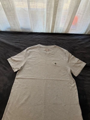 Ljusgrå t-shirt från Morris - Snygg ljusgrå t-shirt från Morris med diskret logga på bröstet och rund hals. Tillverkad i mjuk bomull och har en klassisk passform med korta ärmar. Perfekt basplagg för alla tillfällen.