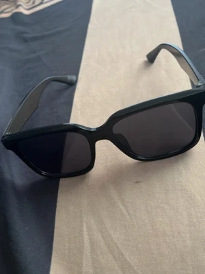 Svarta kantiga solglasögon - Snygga svarta solglasögon med kantig form och breda bågar. Glasen är mörka och ger en cool look som passar till många stilar. Perfekta för soliga dagar och ett måste i accessoargarderoben.