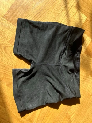 Svarta träningstights-shorts SOC - Säljer ett par svarta träningstights-shorts från SOC. De har en tight passform och är tillverkade i ett stretchigt syntetmaterial som passar perfekt för träning. Klassisk design utan synliga detaljer eller mönster.