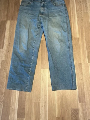 Blå raka jeans från Nudie Jeans - Säljer ett par klassiska blå raka jeans från Nudie Jeans. Jeansen har fem fickor, normal midja och en avslappnad passform. Tillverkade i slitstark denim med Nudie-logga på bakfickan. Perfekta för en casual och trendig look. 54 storlek 