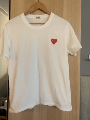 Vit t-shirt Comme des Garçons Play - Vit t-shirt från Comme des Garçons Play med det ikoniska röda hjärtat med ögon broderat på bröstet 