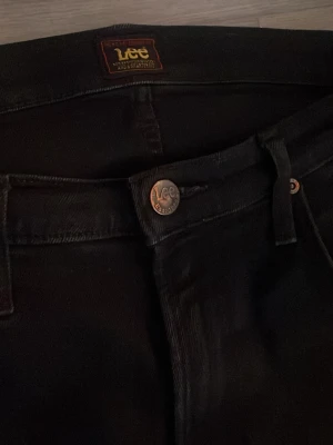 Lee jeans- Daren zip fly  - Säljer ett par svarta jeans från Lee med klassisk femficksmodell och raka ben. Jeansen har Lee-logga på bakfickan och läderpatch i midjan. Tillverkade i slitstarkt denimtyg och har knappgylf framtill. Perfekta för en clean och tidlös look.
