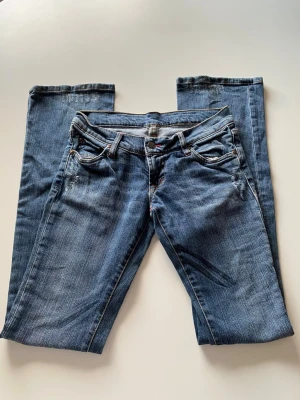 Blåa Puss & Kram jeans med stjärnor - Snygga blå jeans från Puss & Kram med lite utsvängda ben nertill och coola stjärnor broderade på bakfickorna. Klassisk femficksmodell med låg midja och detaljerade sömmar. Perfekta för dig som gillar en avslappnad men trendig stil.