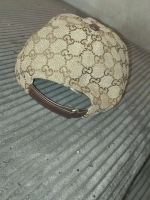 Beige keps från Gucci med GG-mönster - Säljer en beige keps från Gucci med klassiskt GG-monogram över hela kepsen. Kepsen har justerbar rem i brunt läder och en grön-röd rand på sidan. Materialet är canvas och detaljerna ger en lyxig känsla.