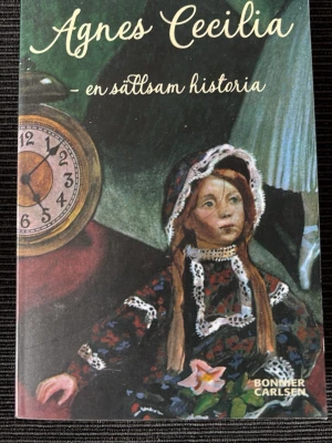 Agnes Cecilia – en sällsam historia - En svensk ungdomsroman av Maria Gripe, pocketutgåva från Bonnier Carlsen. Omslaget har en mystisk illustration med en gammaldags docka och en klocka. Boken är en spännande spökhistoria om Nora och övernaturliga händelser. Perfekt för dig som gillar klassiska mysterier.