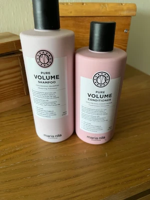 Maria Nila Pure Volume schampo & balsam - Säljer ett set med Maria Nila Pure Volume schampo och balsam. Båda flaskorna är ljusrosa med svarta lock och har en stilren, rundad form. Perfekt för dig som vill ha volymgivande hårvård med veganska ingredienser.