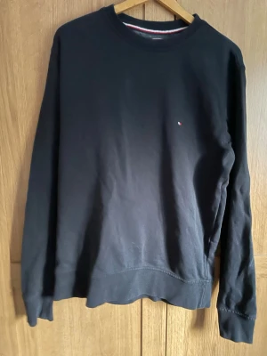 Svart sweatshirt från Tommy Hilfiger - Klassisk svart sweatshirt från Tommy Hilfiger med rund halsringning och diskret logga på bröstet. Tröjan har långa ärmar och ribbade muddar. Perfekt för en avslappnad och stilren look.