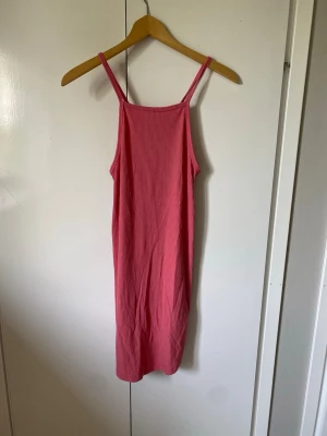Rosa ribbad midiklänning med smala band - En enkel och snygg rosa klänning med smala axelband och rak passform. Klänningen är ribbad och har en mjuk, stretchig känsla. Perfekt för varma dagar och har en stilren look som är lätt att matcha med sneakers eller sandaler.