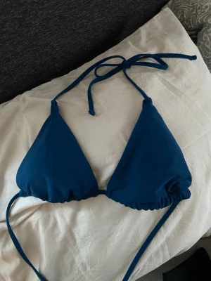 Mörkblå trekantsbikinitopp - Snygg mörkblå trekantsbikinitopp med knyt i nacken och ryggen. Klassisk modell med justerbara band och lätt rynkade kanter nedtill. Perfekt för strand eller poolhäng.