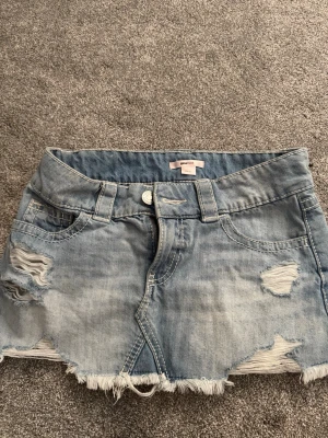 Ljus jeanskjol med slitningar - Jeanskjol från Ginatricot i storlek xs med slitna detaljer och fransig nederkant. Säljer på grund av att den inte kommit till användning, endast använd en gång.