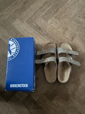 Birkenstock sandaler i mocka - Snygga sandaler från Birkenstock i beige mocka med två justerbara remmar och metallspännen. Klassisk och bekväm modell som passar perfekt till sommaren. Fotbädden är formad för extra komfort och stöd.