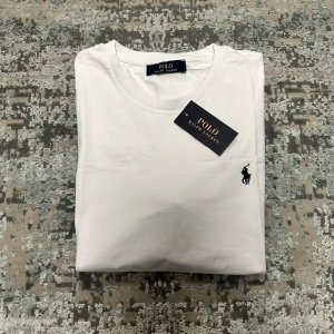 Vit t-shirt - Klassisk vit t-shirt med rund halsringning och korta ärmar. Diskret broderad logga i marinblått på bröstet. Perfekt basplagg i mjuk bomull som passar till allt.