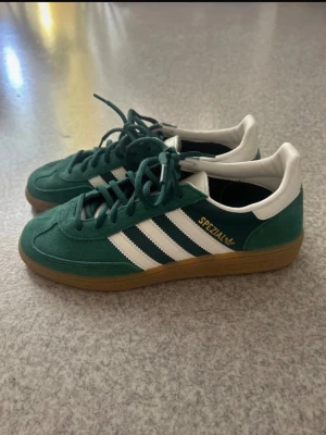 Adidas Spezial gröna sneakers - Gröna Adidas Spezial sneakers med klassiska vita ränder på sidorna och vit häl. Ovandel i mocka och detaljer i läder, samt gummisula i brunt. Snygg retrostil med guldfärgad Spezial-logga på sidan. Perfekta för dig som gillar streetwear och sportig look.