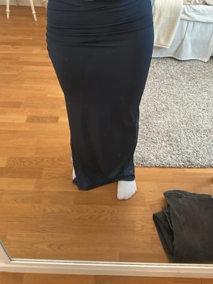 Mörkblå långkjol med slits - Snygg mörkblå långkjol med slits på sidan. Kjolen har en tight passform och är tillverkad i ett stretchigt material som sitter skönt på! Perfekt för dig som gillar en stilren och trendig look.
