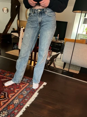 Blå raka jeans med hög midja - Snygga blå jeans med rak passform och hög midja. Jeansen har klassisk femficksdesign och stängs med knapp och dragkedja. Perfekta för en avslappnad och trendig look. 