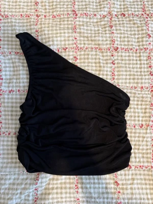 Svart oneshoulder topp från Pieces - Snygg svart oneshoulder topp från Pieces i mjukt och stretchigt material. Toppen har en asymmetrisk design med rynkade detaljer på sidorna.