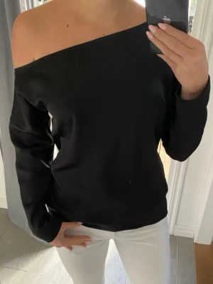 Svart offshoulder top  - Snygg svart offshoulder topp med lång ärm. Toppens enkla design gör den lätt att matcha och den har en stilren, rak passform. Materialet känns mjukt och följsamt mot huden.