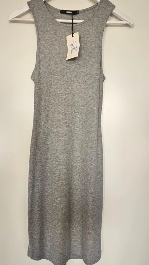 Grå ribbad klänning från Bik Bok - En enkel och stilren grå ribbad klänning från Bik Bok. Ärmlös modell med rund halsringning och rak passform. Perfekt att styla med sneakers eller boots för en avslappnad look. Ny med prislapp.