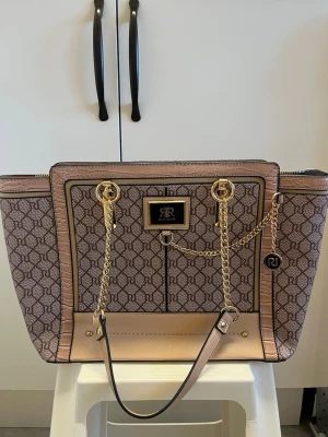 River Island väska - Stor väska från river island i gott skick. Ca 43cm bred och 27cm hög. Guldfärgad metall och Innehåller flera fack.