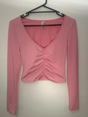 Rosa långärmad topp med rynk framtill - Snygg rosa långärmad topp ifrån Nelly,med v-ringning och rynkade detaljer framtill. Modellen är croppad och har en figurnära passform. Perfekt att styla med jeans eller kjol för en trendig look.💕