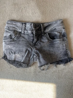 Grå jeansshorts LTB - Snygga grå jeansshorts med slitna detaljer och fransig kant nertill. Klassisk femficksmodell med bälteshällor och knappgylf. Perfekta för en avslappnad stil under varma dagar.