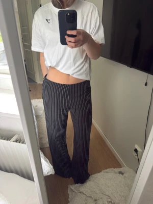 Svarta kostymbyxor med vita ränder - Snygga svarta kostymbyxor med vita smala ränder i klassiskt pinstripe-mönster. Byxorna har rak och något utsvängd passform med låg midja. Storlek 40 men passar mig som vanligtvis har 34!