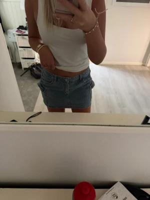 Blå jeanskjol med fickor - Snygg blå jeanskjol i kort modell med klassiska fickor fram och bak. Kjolen har en enkel design med knapp och dragkedja framtill. Perfekt för dig som gillar en avslappnad och trendig stil. Storlek 40 men är mer en 38