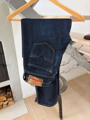 Mörkblå jeans Diesel - Snygga mörkblå jeans från Diesel med klassisk femficksdesign och kontrastsömmar. Jeansen har en ganska rak passform men är lite mer mot bootcut hållet, är tillverkade i slitstarkt denimtyg. Väldigt bekväma och har varit mina favoriter men säljer dem då de inte passar mig längre.