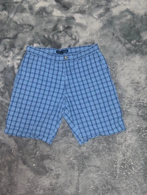 Tommy Hilfiger Rutiga Chino-shorts -  ett par klassiska rutiga shorts från Tommy Hilfiger i olika blå nyanser. Sjukt snygga till sommarn! Skick: 10/10 inga defekter. • Detaljer: Gylf med knapp och dragkedja, fickor både fram och bak