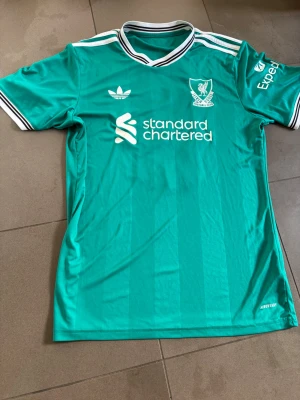 Liverpool bortatröja Szoboszlai #8 - Säljer Liverpools gröna bortatröja från Adidas med Szoboszlai på ryggen. Tröjan är i nyskick och köptes för 1200 kronor hos adidas