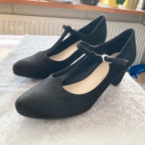 Svarta klackskor strl 41 - Ett par svarta klackskor i en klassisk, vintage stil, strl 41. Har använts max 3 ggr och är därmed i bra skick. På utsidan är skorna gjorda av ett mjukt faux mockamaterial. Nypris ca 300 kr.