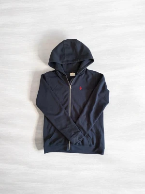 Mörkblå hoodie från Polo Ralph Lauren - Snygg mörkblå hoodie med dragkedja från Polo Ralph Lauren. Klassisk design med huva och röd broderad logga på bröstet. Tillverkad i mjukt bomullsmaterial och har två fickor framtill. Perfekt för en avslappnad och stilren look. Priset kan diskuteras. Med vänlig hälsning, Valter ☺️