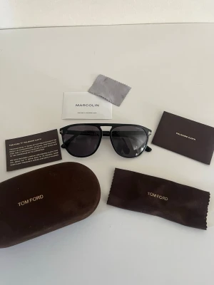 Svarta solglasögon från Tom Ford - Snygga svarta solglasögon från Tom Ford med klassisk pilotform och mörka glas. Bågarna är i svart och har den ikoniska T-detaljen i guld vid sidorna. Kommer med originalfodral, putsduk och certifikat. Har en skråma på insidan som BARA syns från insidan, påverkar inte lensen eller syns ej vid använding. Skickar till sverige 🇸🇪