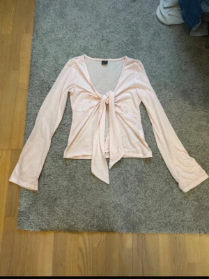 Ljusrosa omlottopp från Gina Tricot - Supersöt ljusrosa omlottopp från Gina Tricot med långa ärmar och knyt framtill. Tunt och mjukt material som känns skönt mot huden. Perfekt att styla med jeans eller kjol för en trendig look.