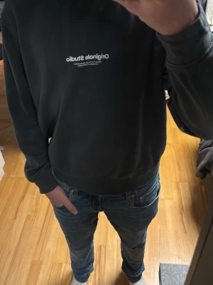 Gröngrå sweatshirt Originals Studio - Gröngrå sweatshirt från Originals Studio med vit logga tryckt på bröstet. Tröjan har rund halsringning, långa ärmar och ribbade muddar vid ärmslut och nederkant. Perfekt för en avslappnad och stilren look.