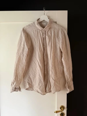 Beige linneskjorta med lång ärm - Snygg beige skjorta i linne med klassisk krage och långa ärmar. Skjortan har knäppning framtill och en avslappnad passform, perfekt för en stilren och enkel look.