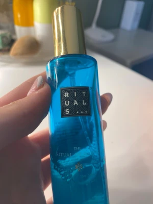 Rituals blå parfymflaska - Snygg parfym från Rituals i en genomskinlig blå flaska med guldfärgat lock. Flaskan har en stilren och modern design med Rituals logga framtill. Perfekt att ha på sminkbordet eller i väskan för en fräsch doft när du vill. Pris kan diskuteras och använd fåtal ggr